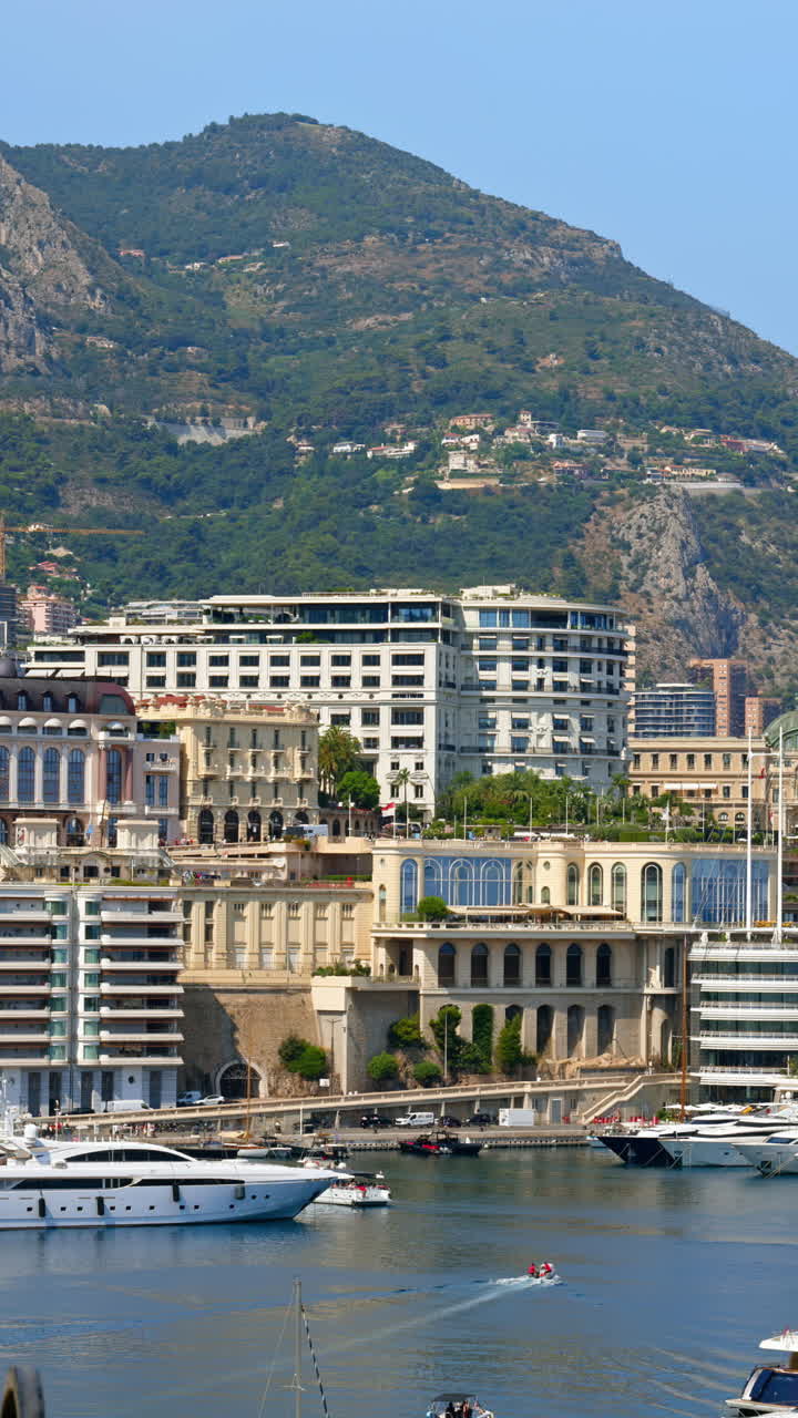 View of boats docked in the Monaco Marina with the skyline of the city on the background. Vertical