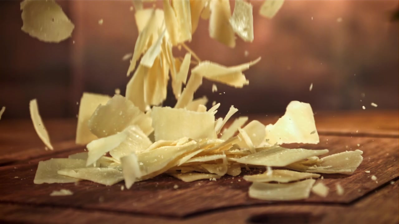 Copeaux de parmesan tombant sur une planche à découper en bois au ralenti