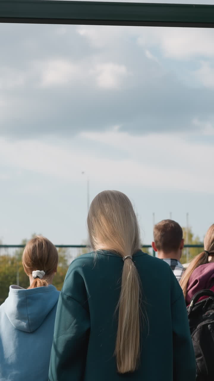 배경에는 축구장과 나무가 보이는데, 코치가 게이트를 열고 볼리볼 코트에 들어오는 젊은이들의 뒷모습, 활동적인 생활 방식을 강조합니다.