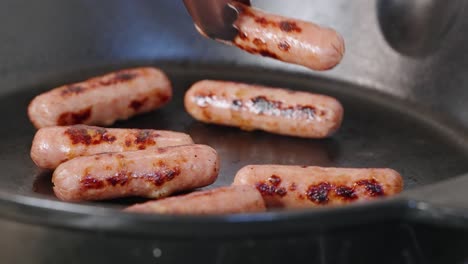 tongs reach into hot pan of cooked breakfast sausages and grab one with grill marks to plate