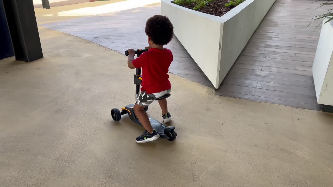 Exotic, bold and adoirable two year old african european child happy riding his first skateboard