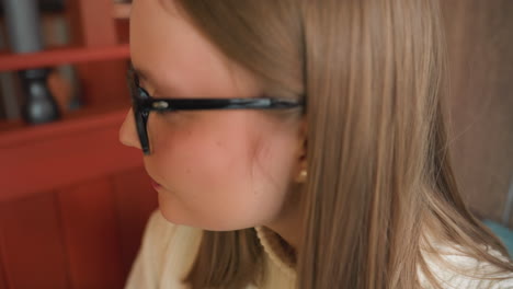 close up of woman in glasses eating slice of chocolate cake with gold fork by wooden frame background, lips open biting cake conveying cozy cafe indulgence and warm lighting illuminating scene