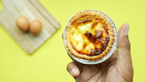 top view of holding a egg tart against yellow background ,