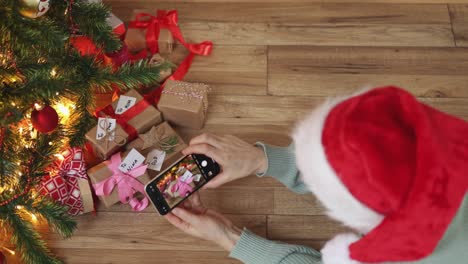 sombrero de navidad rojo femenino manos de teléfono inteligente pantalla verde bajo cajas de regalos de abeto