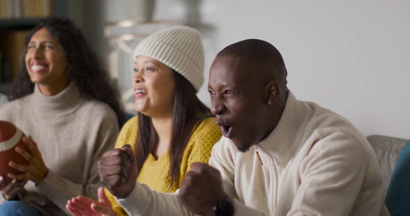 Afro-Amerikaanse vrienden reageren op tv op de bank, de man rechts wijst en gebaart naar een voetbalwedstrijd, met vrije ruimte.