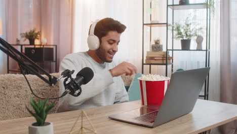 young indian man streaming football match commentary eating popcorn and engaging audience at home