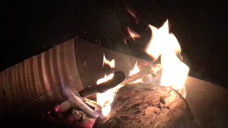 handheld shot of large log burning in giant box fire pit, nighttime