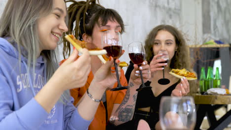 happy female friends eating pizza and drinking wine at home