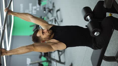 vídeo vertical de un hombre entrenando los músculos de la espalda y las manos haciendo ejercicios con pesas en un gimnasio