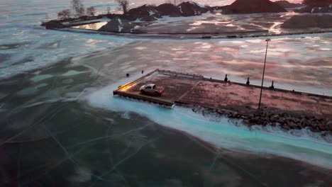 Orbiting-over-a-ferry-and-around-a-pickup-truck-sitting-at-the-end-of-a-dock-surrounded-by-the-frozen-lake-during-winter-in-Canada