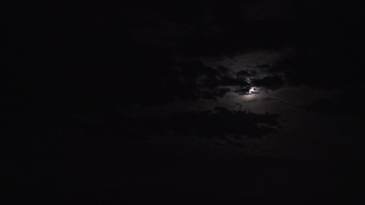 Aerial footage capturing the ethereal beauty of a super moon obscured by dramatic night clouds. The moon's glow creates a mystical ambiance, enhanced by the expansive, silent sky