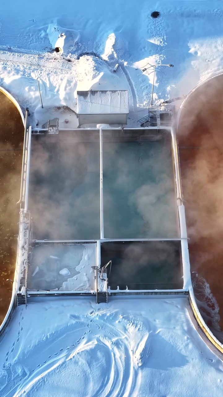 Ripresa aerea dall'alto di un impianto industriale di depurazione delle acque con denso vapore che sale dai serbatoi durante una fredda giornata invernale. Utile per temi di sostenibilità e infrastrutture industriali