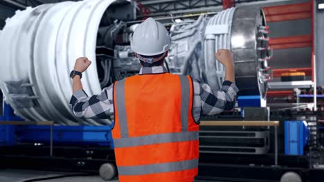 back view of a male engineer with safety helmet raising his hands celebrating while working with airplane engine maintenance conducted, analytics checking the turbine