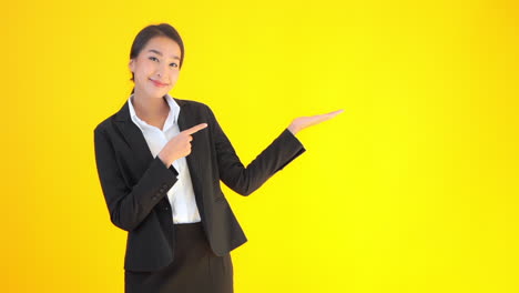 a well dressed young woman raises her hand palm down for presentation and points to the blank space with the other