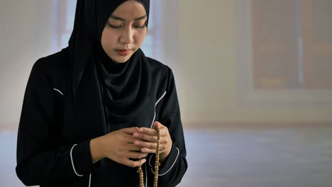 asian muslim young woman in black traditional hijab praying with islamic beads in mosque.