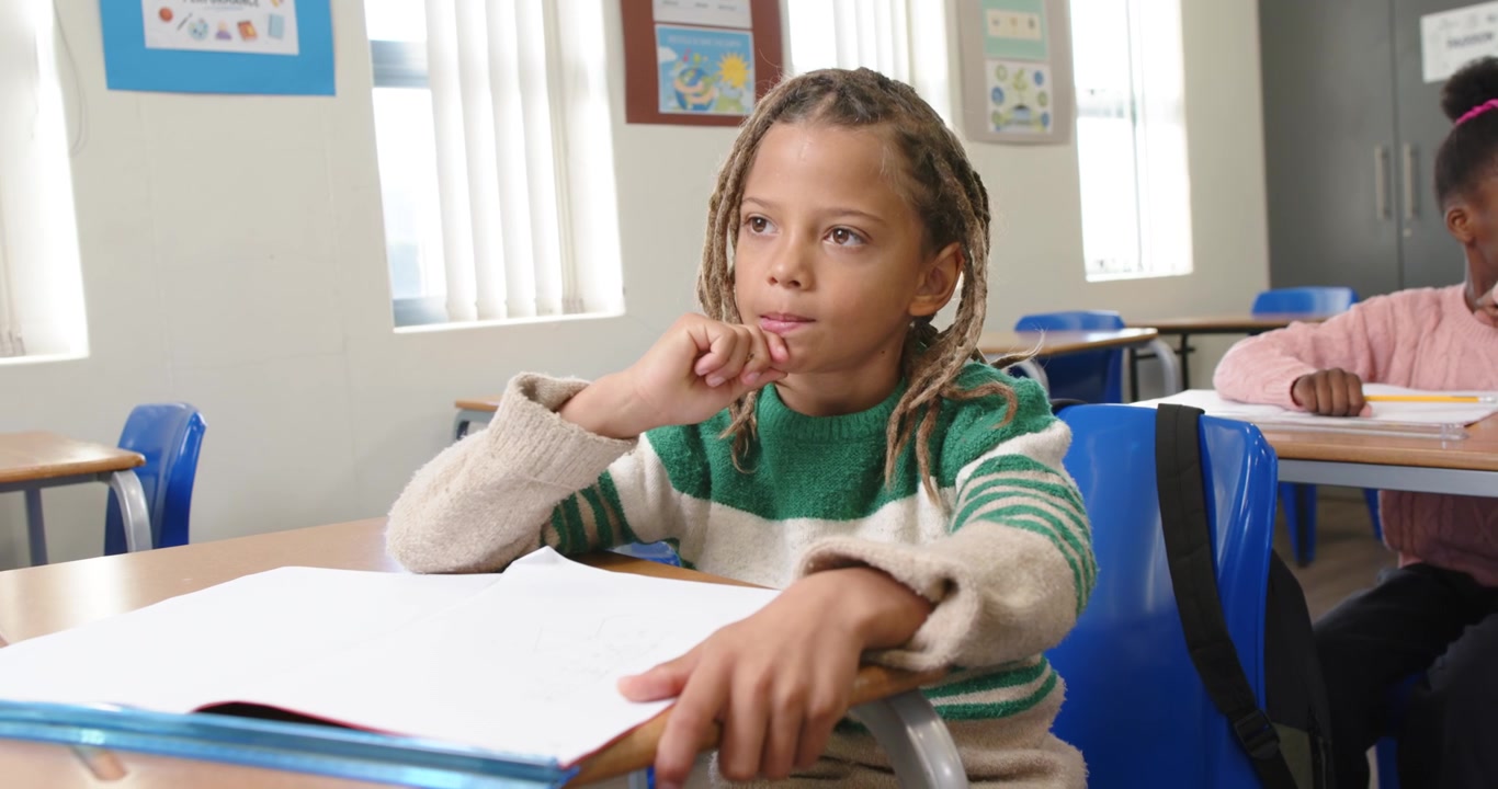 Ragazze afroamericane a scuola, una bambina con maglietta verde che scrive sul quaderno con la matita, in pausa.