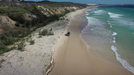 Rotating-aerial-tracks-truck-driving-on-sunny-soft-sandy-ocean-beach