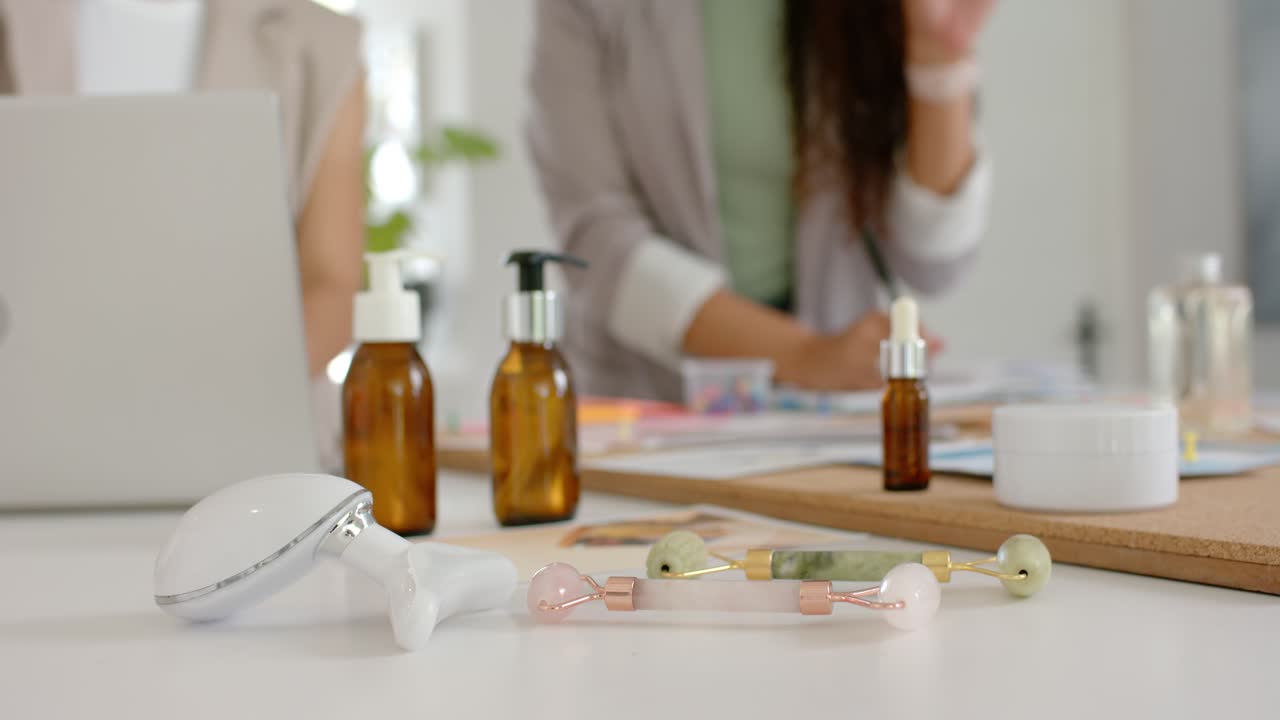 Strumenti per la cura della pelle che rimangono centrati sul tavolo mentre due donne iniziano a parlare, indicando e prendendo nota del design