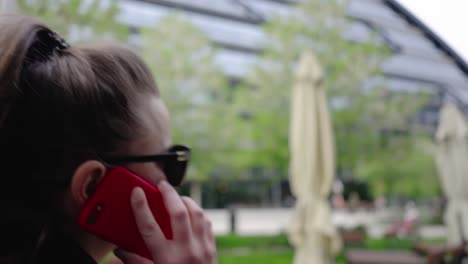 close-up of a woman talking on the phone while walking past glass office buildings