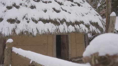 rustic hut with a thatched roof stands covered in snow, nestled in a quiet winter village.