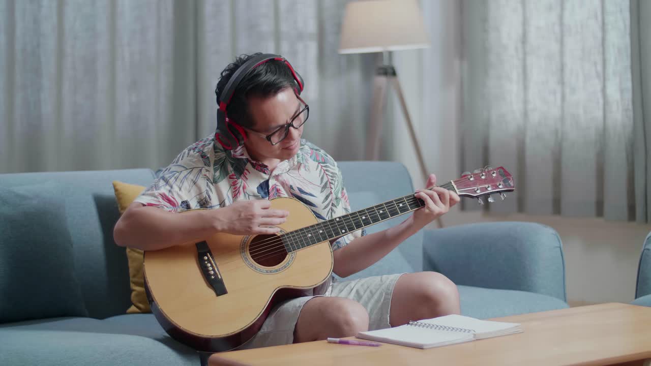 집에서 기타를 연주하는 헤드폰을 착용한 테이블에 노트북을 가진 아시아인 작곡가