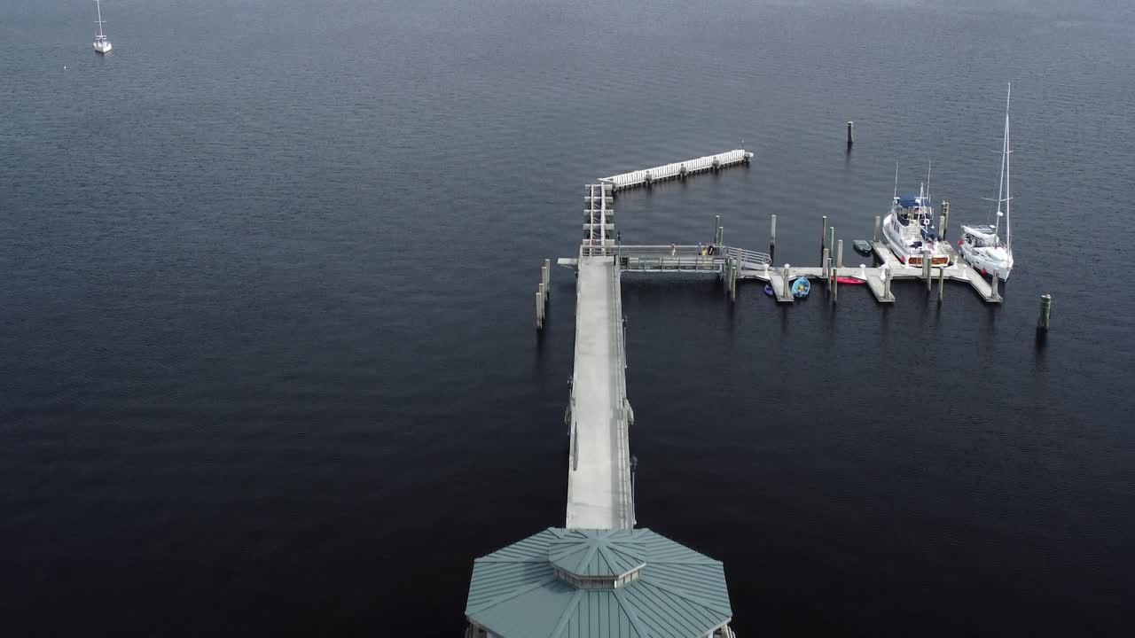 A stunning drone shot glides over a scenic pier extending into a tranquil river, capturing the serene waters and lush surroundings.