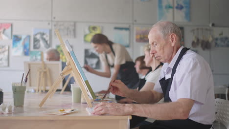 side view of a happy senior people smiling while drawing as a recreational activity or therapy in paint class together with the group of retired women and men