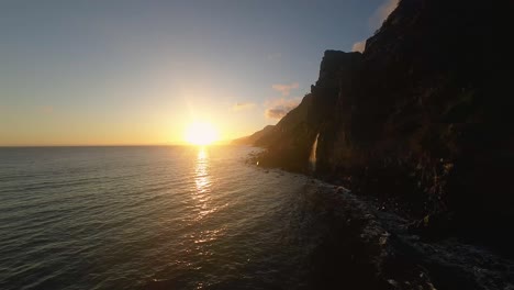 Coastal-cliffs-line-the-sea-with-bright-orange-sunset-near-horizon-in-distance