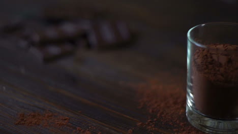 Dark-chocolate-bar-and-cacao-powder-in-glass-on-wooden-table.-Chopped-chocolate