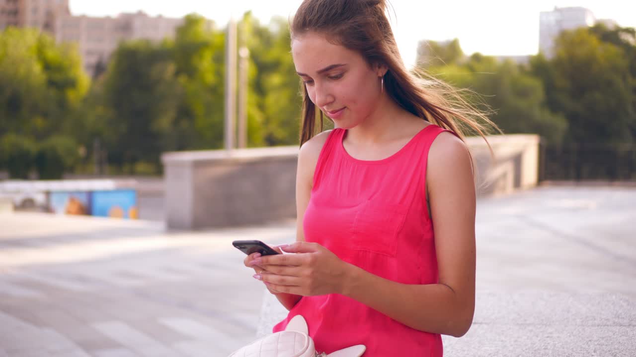 chica feliz sonriendo mientras envía mensajes de texto en su teléfono inteligente en el centro de la ciudad