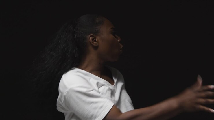 Primer plano de estudio de mujer joven bailando con iluminación de clave baja contra un fondo negro.
