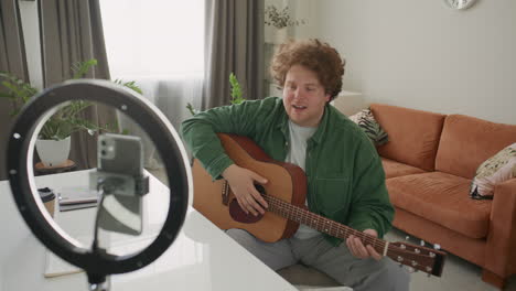 young man recording guitar lesson with ring light and phone at home