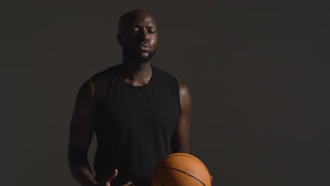 Studioporträtaufnahme-Eines-Männlichen-Basketballspielers,-Der-Vor-Dunklem-Hintergrund-Den-Ball-Von-Hand-Zu-Hand-Wirft