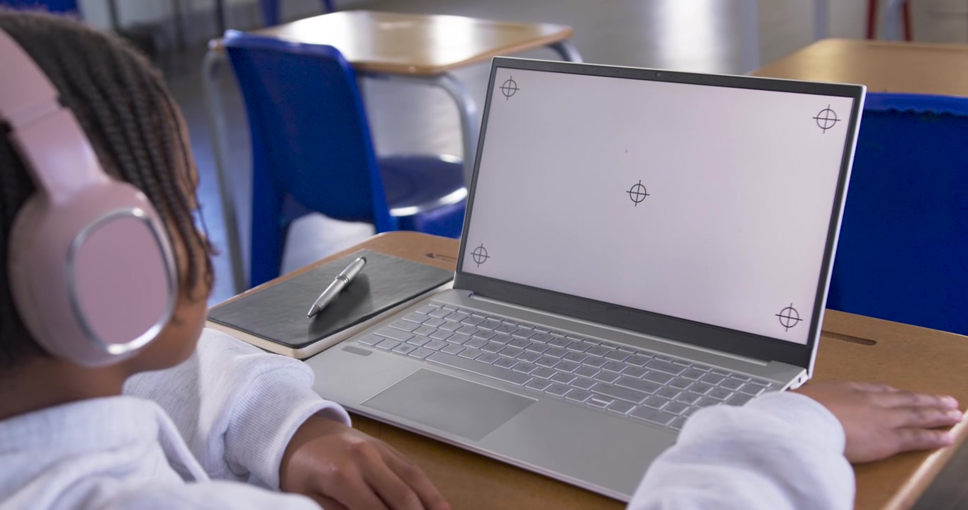 Giovane uomo africano seduto a sinistra a un banco di scuola, con cuffie rosa, che studia al portatile, con spazio per il testo