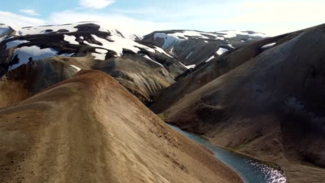 Flight-over-golden-mountains-and-glacier-lake-revealing-a-white-stream-in-a-narrow-gorge-between-steep-slopes