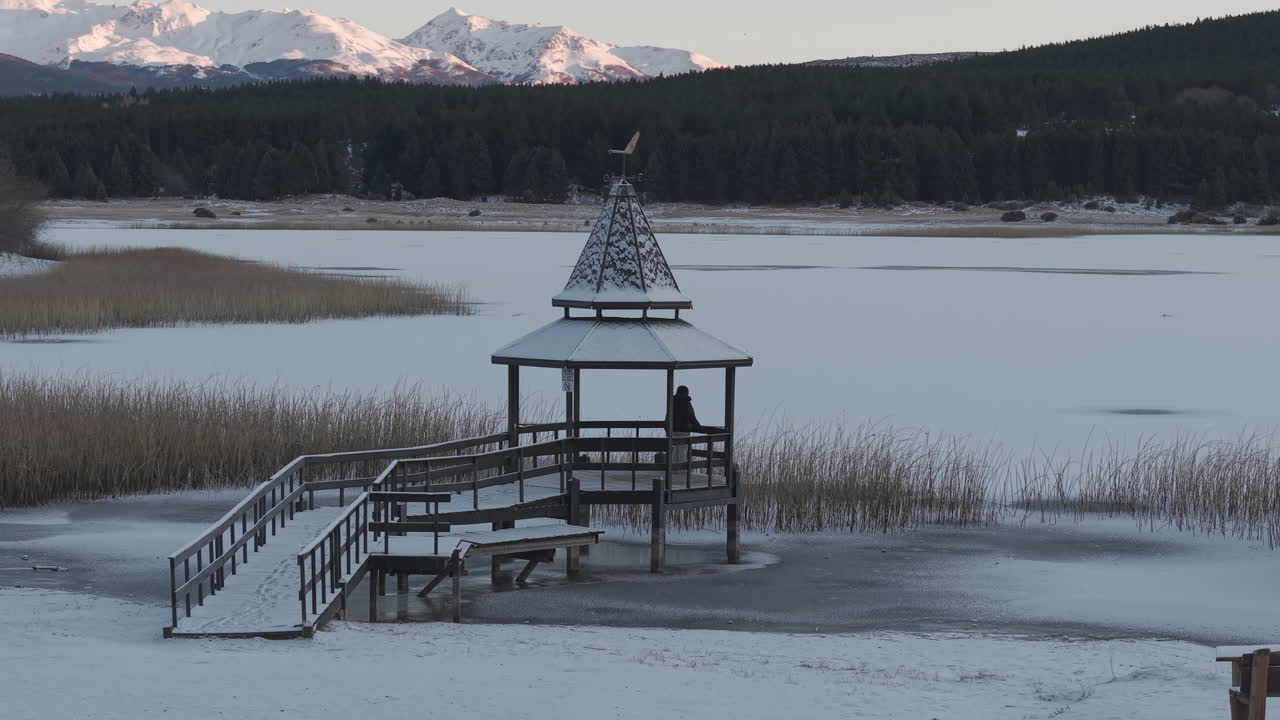 Woman standing on wooden pier by frozen Laguna La Zeta with snowy mountains in Patagonia