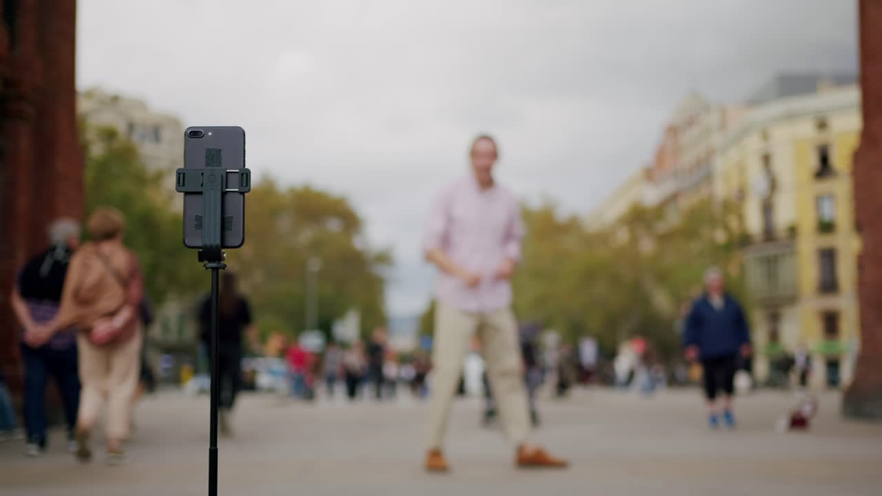 Sokakta internet blogu için dans ederek selfie çubuğu ve akıllı telefonla video çeken erkek blogger. Genç turist, İspanya'nın Barcelona şehrinde dışarıda yürürken cep telefonuyla görüntülü görüşme yapıyor.