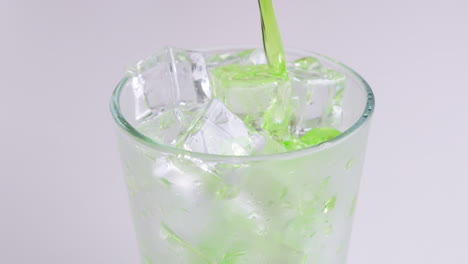 pouring soft drinks and green soda into glass isolated o white background