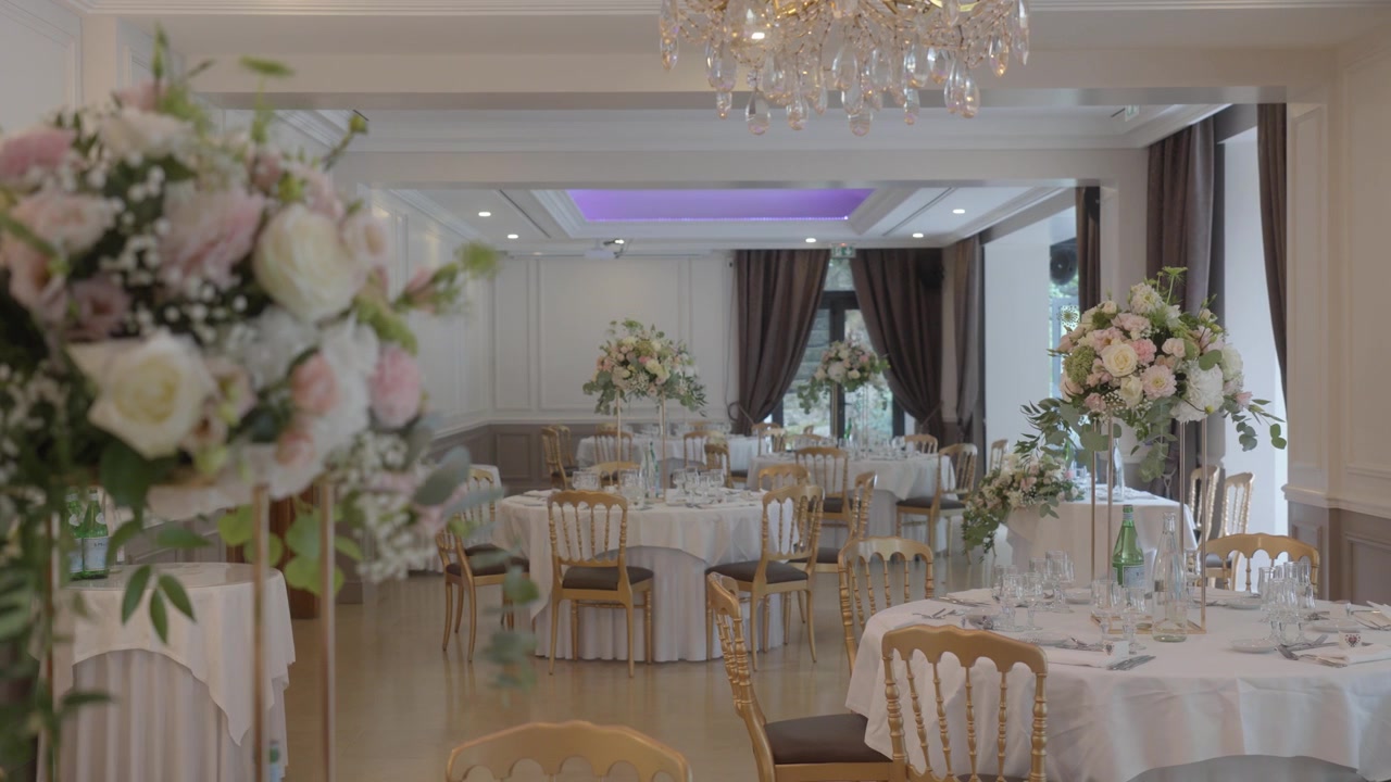 Elegante salón de banquetes preparado para un evento con centros de mesa florales y candelabros.