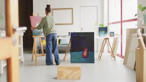 video of back view of biracial female artist painting in studio