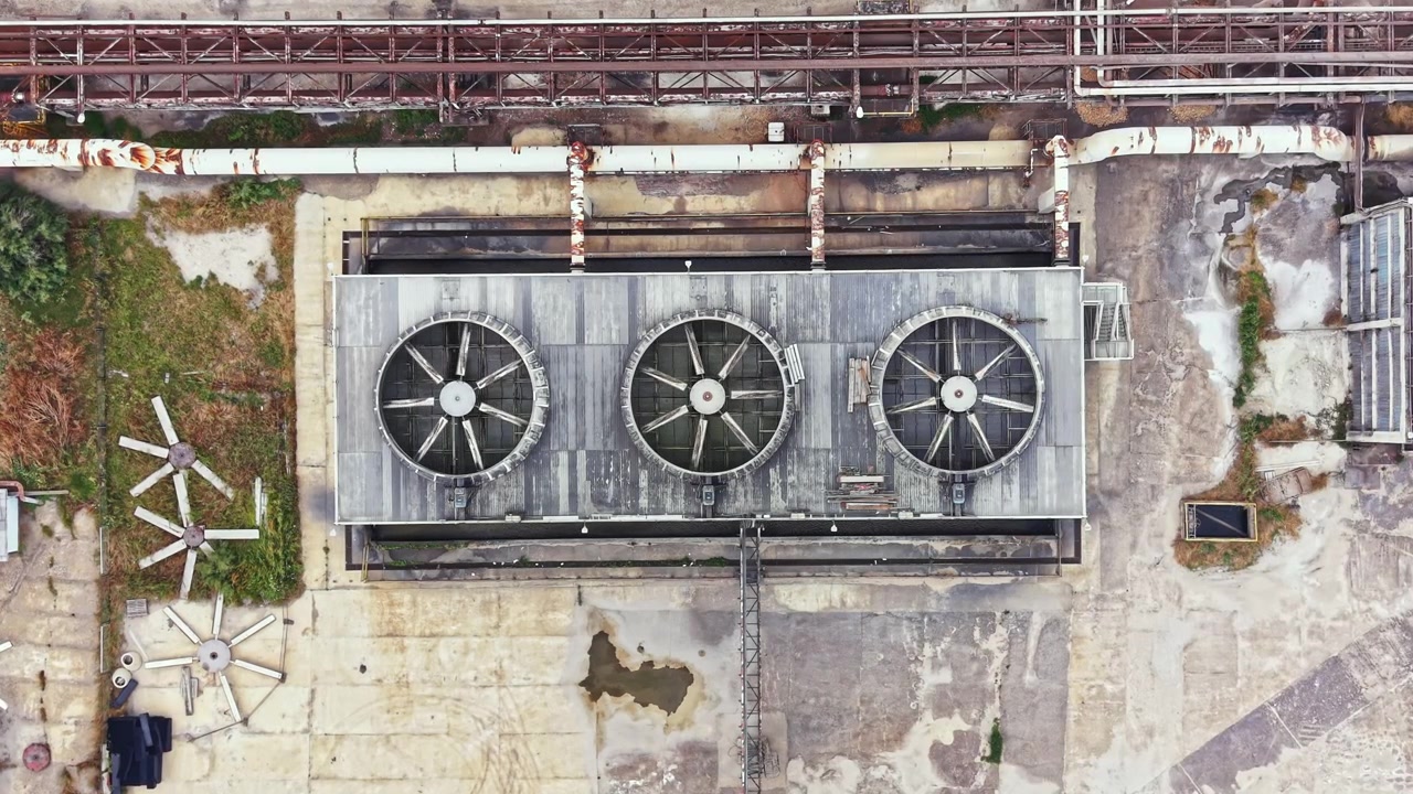 Large industrial rooftop with three cooling fans located in an urban area during daytime showing signs of wear and age