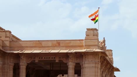 Die-Flagge-Des-Königreichs-Weht-Am-Oberen-Ende-Des-Palasteingangstors-Aus-Rotem-Stein-Bei-Tag-Aus-Einem-Flachen-Winkel.-Das-Video-Wurde-Im-Umaid-Bhawan-Palast-In-Jodhpur,-Indien,-Aufgenommen