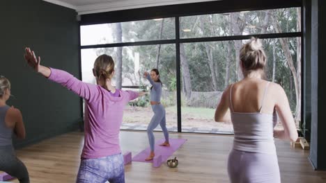 Focused-diverse-women-stretching-together-on-mats-in-yoga-class-with-female-coach,-slow-motion