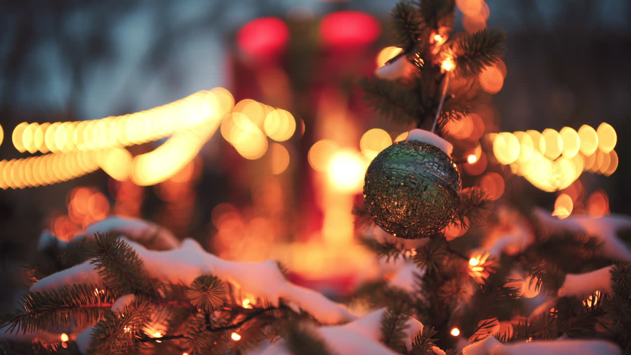 Lähikuva pyöreästä joulupallosta roikkumassa lumipeitteisellä ikivihreällä oksalla.