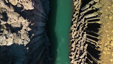 Aerial-drone-top-down-shot-over-scenic-icelandic-studlagil-canyon-with-river-flowing-into-basaltic-rock-formation-in-Iceland-on-a-sunny-day