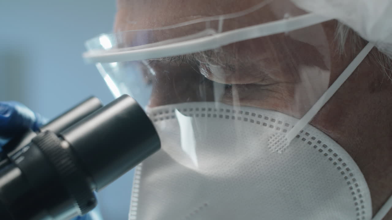 Scienziato senior in uniforme protettiva che osserva al microscopio