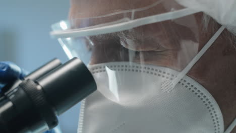 senior scientist in protective uniform looking through microscope