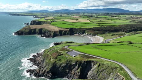 die irische küste stellt eine luftaufnahme der copper coast drive road dar, die in die kilmurrin cove fährt und sich an einem sommermorgen den weg in die comeragh mountains bahnt.