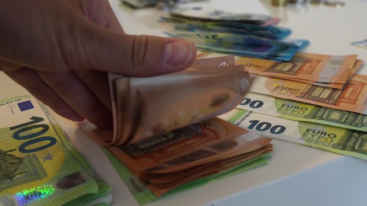 Nahaufnahme einer kaukasischen Daumenbewegung, die durch europäische Euro-Geldscheine auf einer Tischplatte blättert