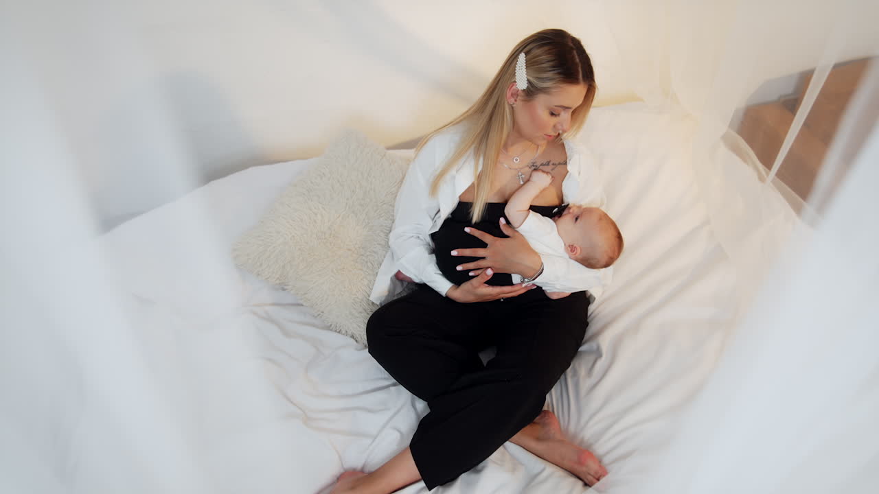 Mother with newborn child sits on the canopy bed with. Caring mom dandling her child. Top view.